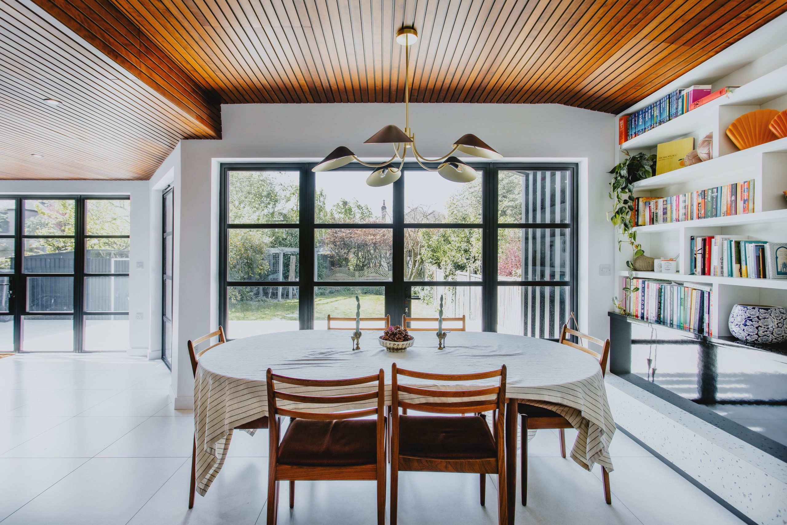 Dining area framed by black steel-look glazed screens overlooking the garden